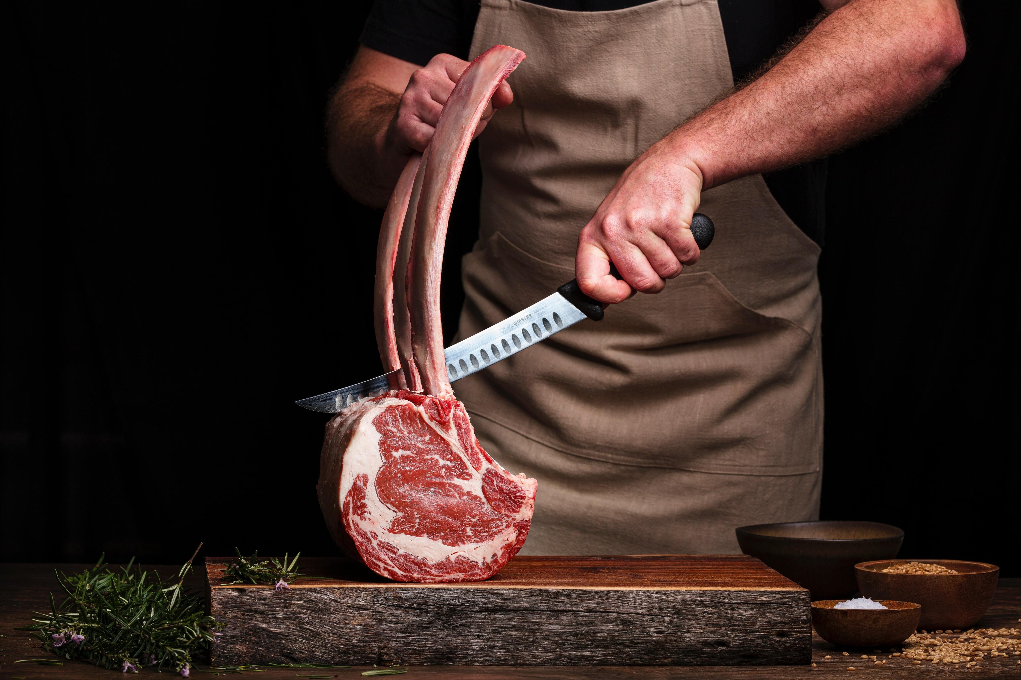 Person holds a sharp knife over large cut of meat